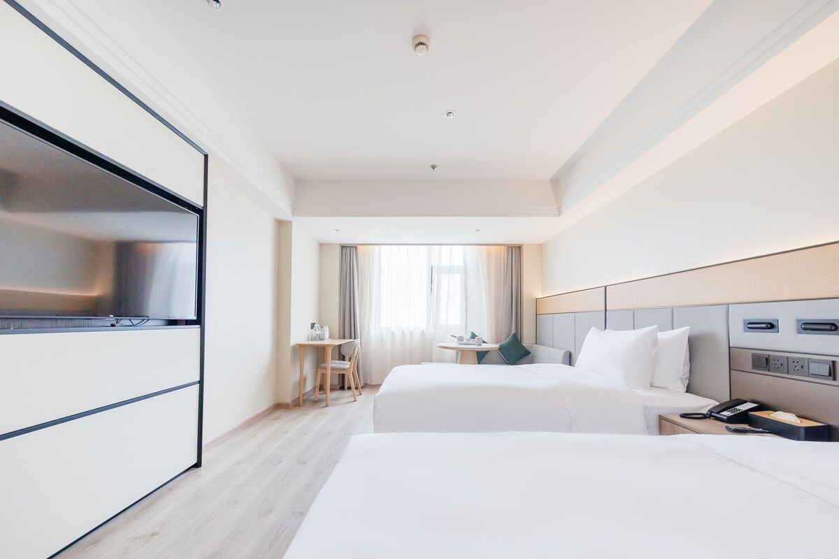 Quarto de hotel com duas camas, uma escrivaninha, uma cadeira, uma TV e um telefone.