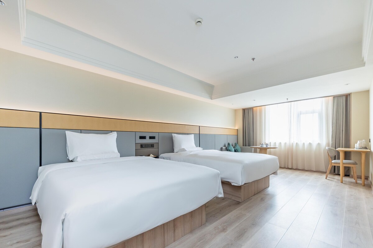 Quarto de hotel com duas camas, uma escrivaninha e uma cadeira.