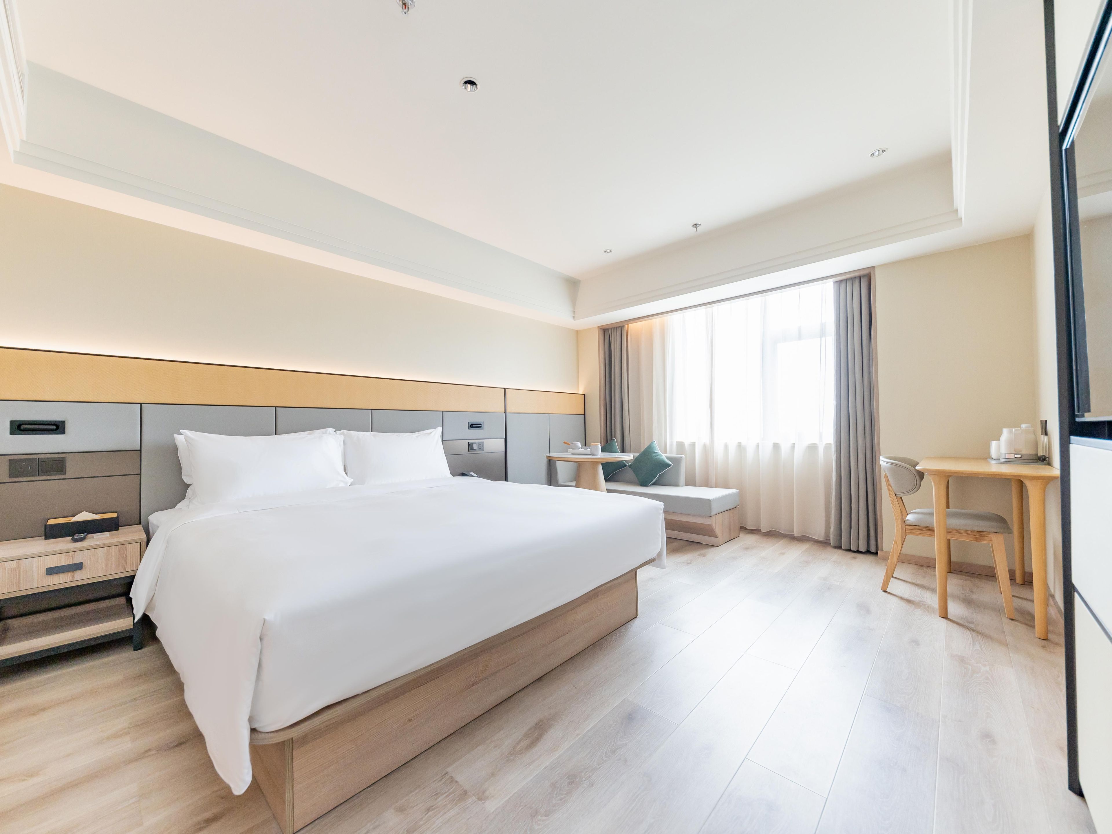 A hotel room with a large bed, bedside table, desk, chair, and a TV.