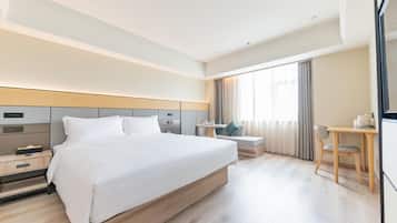 A hotel room with a large bed, bedside table, desk, chair, and a TV.