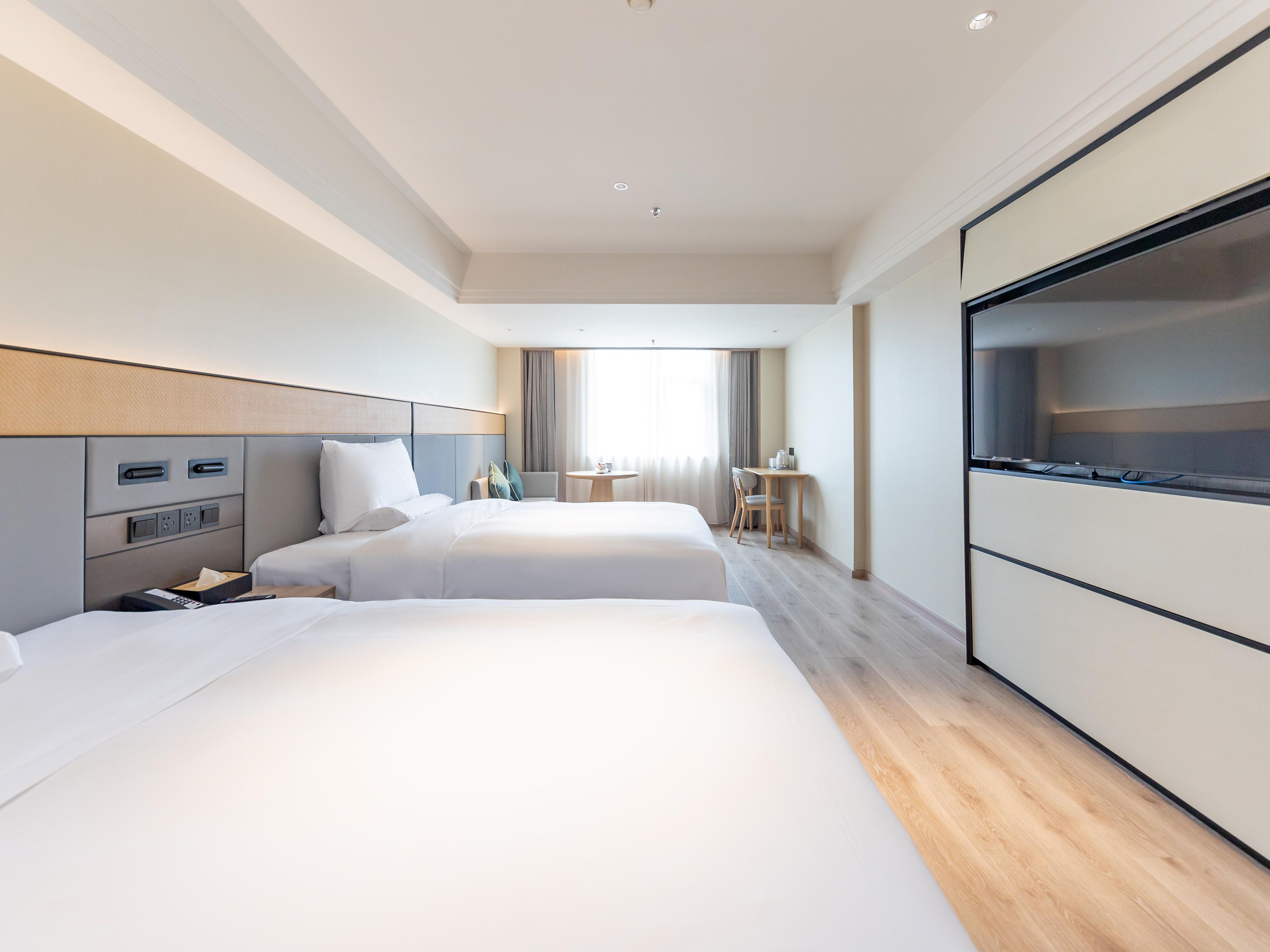A hotel room with two beds, a desk, a chair, and a TV.