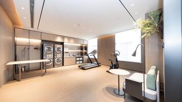A modern hotel room with a large window, a treadmill, a massage chair, and a built-in washer and dryer.