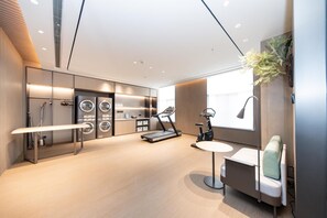 Une chambre d’hôtel moderne dotée d’une grande fenêtre, d’un tapis de course, d’un fauteuil massant et d’un lave-linge et d’un sèche-linge intégrés.