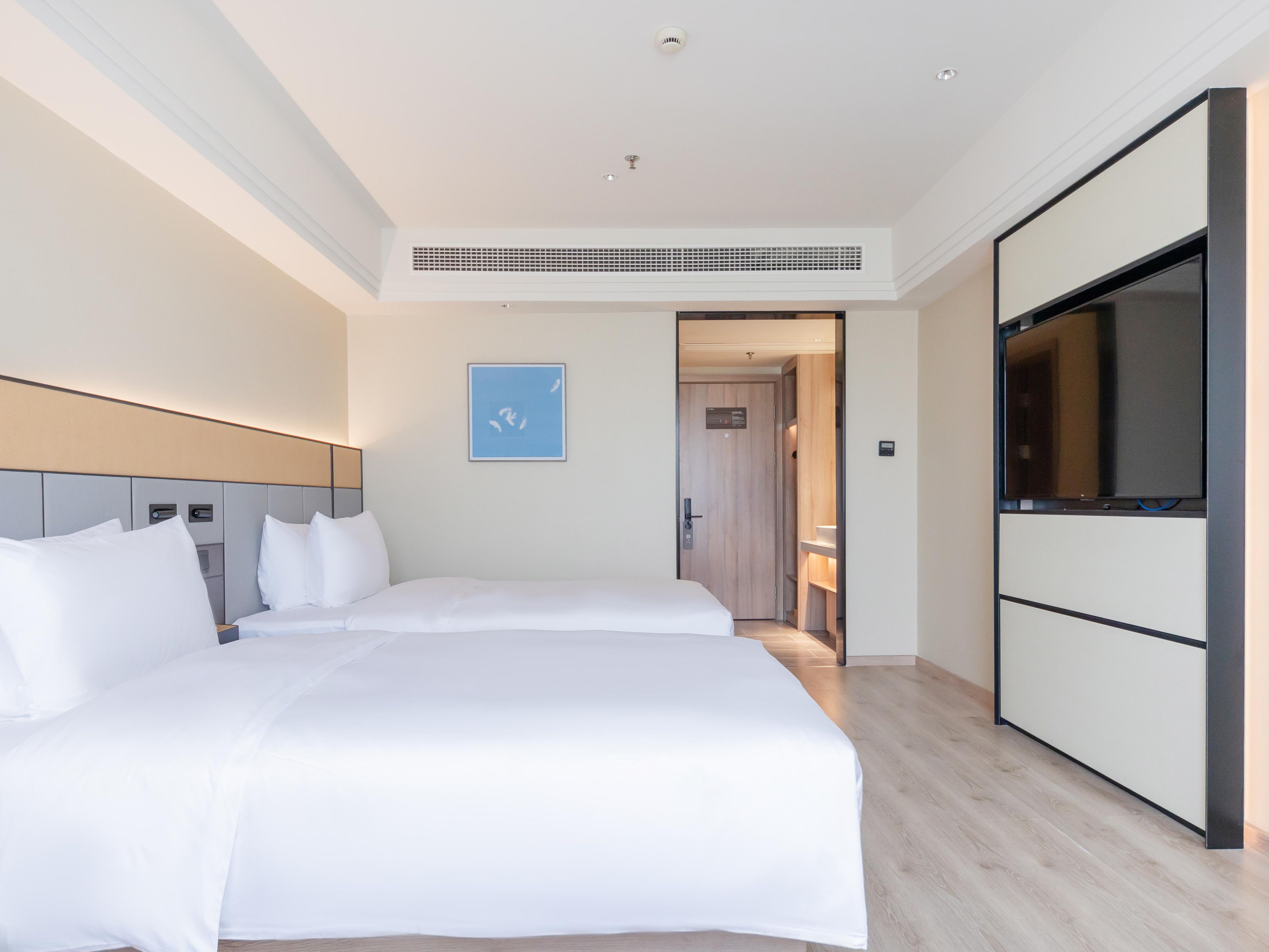 Ein Hotelzimmer mit einem großen Bett, einem Fernseher, einem Schrank und einer Tür zu einem weiteren Raum.