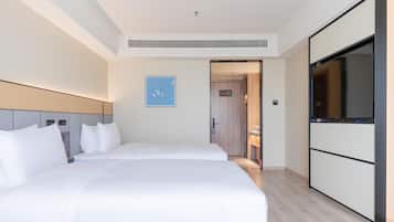 Ein Hotelzimmer mit einem großen Bett, einem Fernseher, einem Schrank und einer Tür zu einem weiteren Raum.