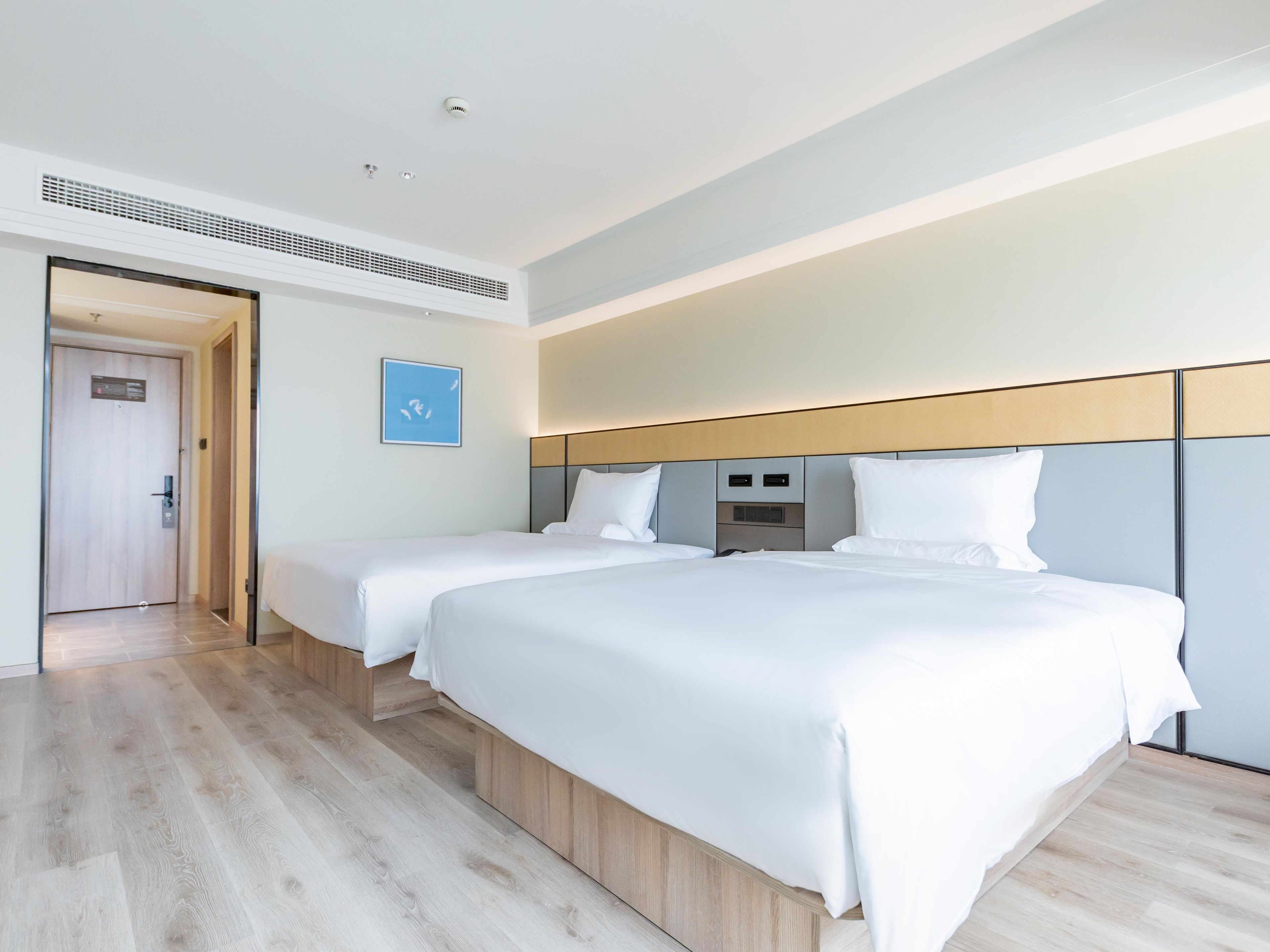 A hotel room with two beds, a wooden floor, a white wall, and a door.