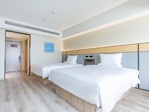 A hotel room with two beds, a wooden floor, a white wall, and a door.