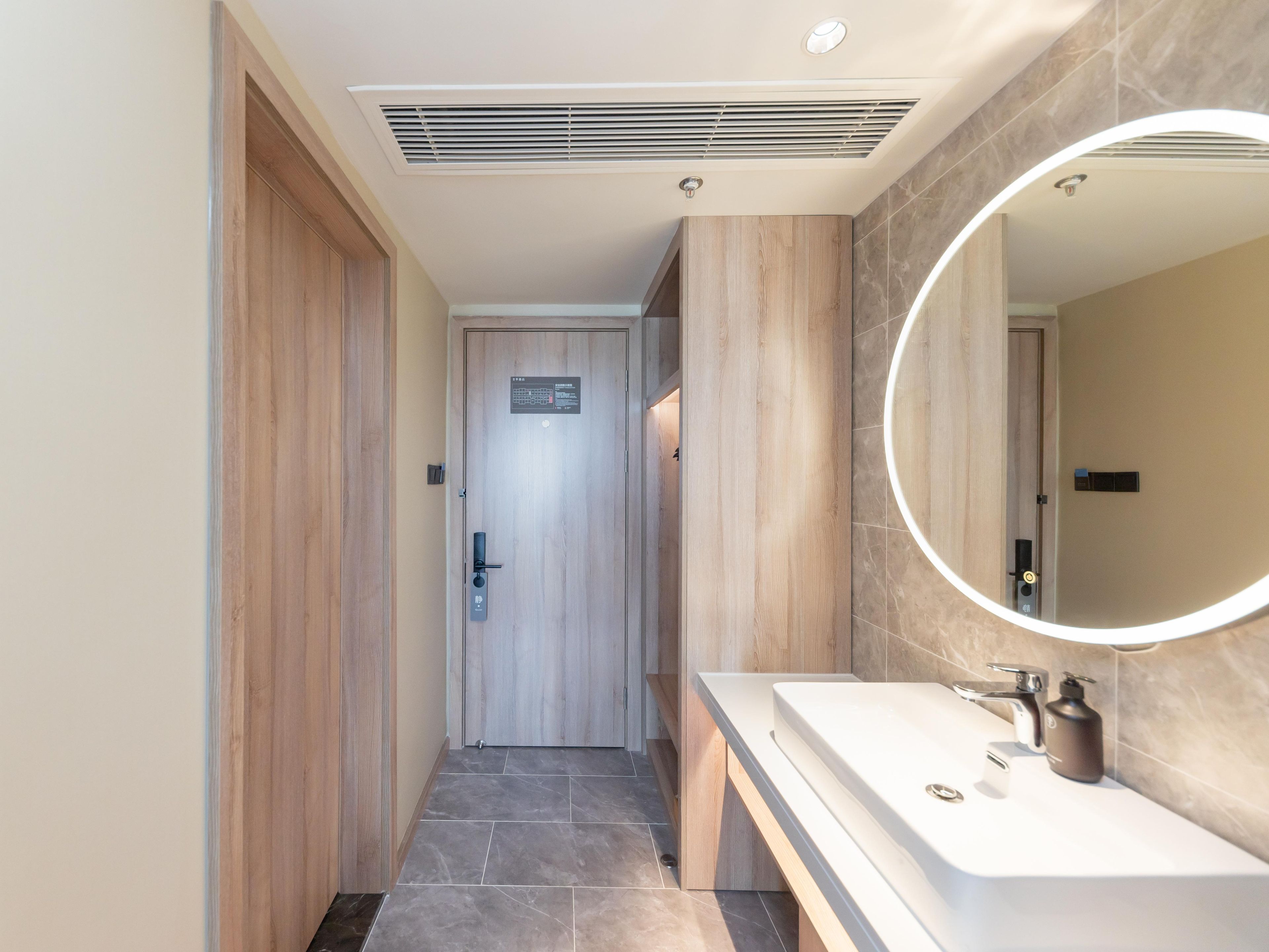 A modern bathroom with a wooden door, a vanity with a mirror, and a shower area.