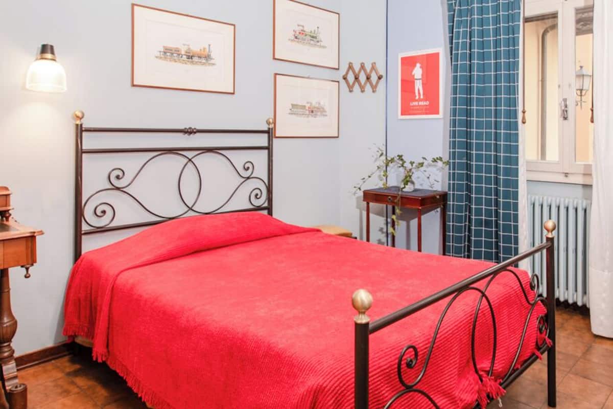 Une chambre à coucher avec un lit, une commode en bois, une table de chevet, un miroir et des tableaux encadrés accrochés au mur.