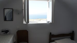 Un dormitorio con una cama individual, una silla, una mesita y una ventana con vistas al mar.