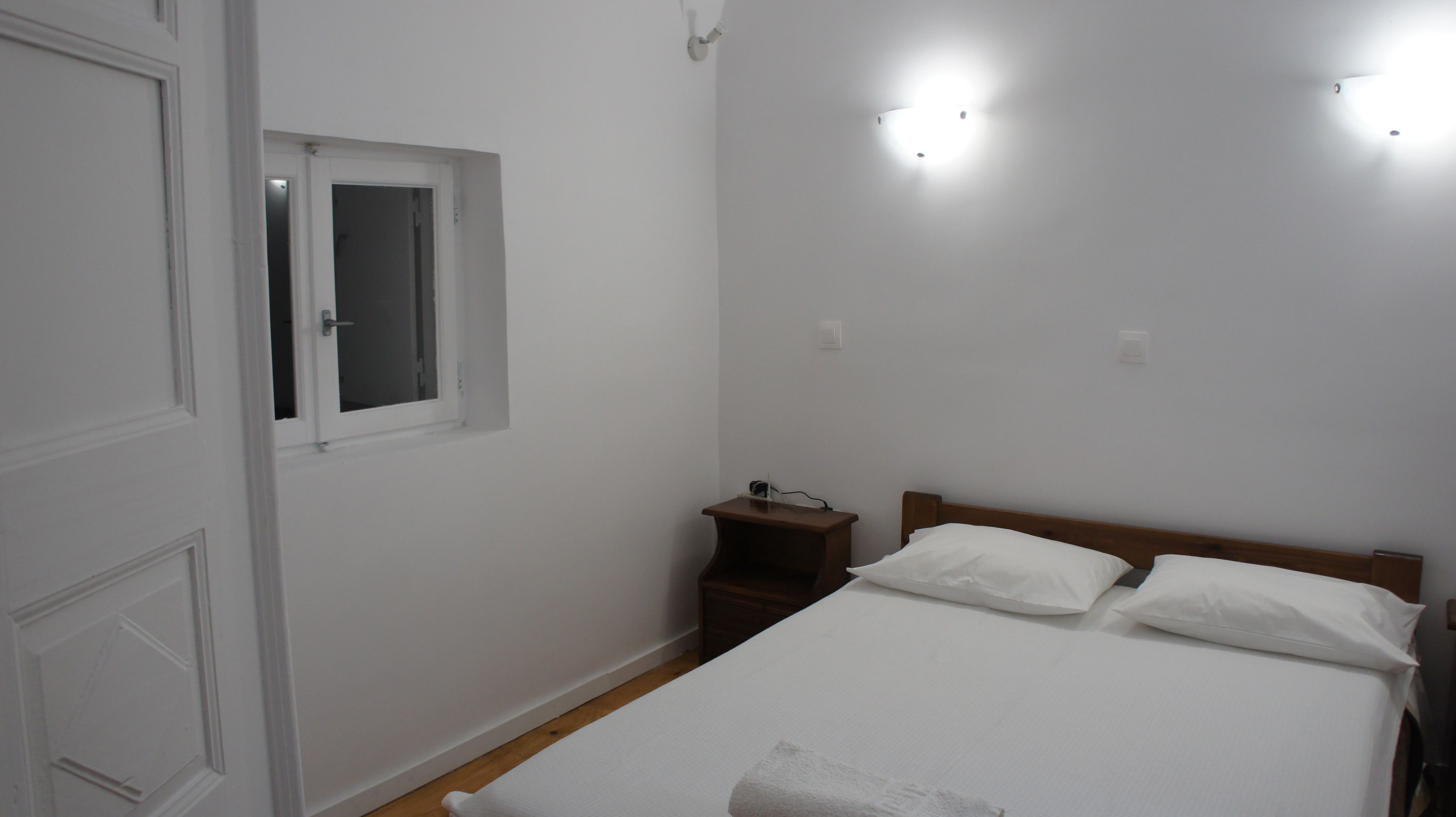 Une chambre à coucher avec un lit, une table de chevet, une fenêtre et une porte.