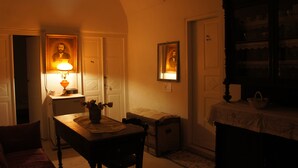 Una habitación tenuemente iluminada con una mesa, sillas, una lámpara y retratos enmarcados en la pared.