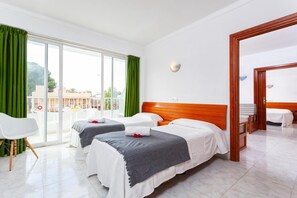 Une chambre d’hôtel avec deux lits, un balcon avec des rideaux verts, une chaise blanche et une porte en bois.