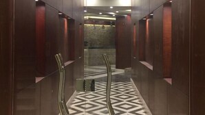 En modern hissinredning med ett golv i geometriskt mönster, metalliska handräcken och en skylt med texten ”Grand Palace Hotel”.