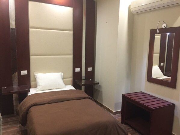 A hotel room with a bed, a nightstand, a small table, a mirror, and a wall-mounted shelf. - Grand Palace Hotel (Cairo)