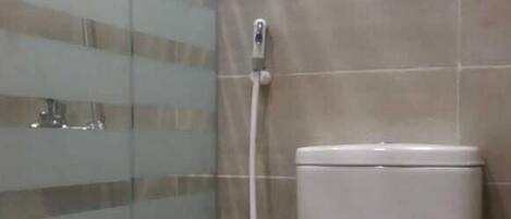 A bathroom with a glass shower enclosure, a toilet, and a wall-mounted faucet.