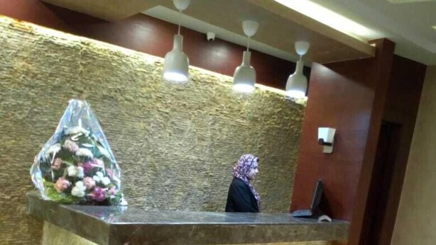 En receptionsdisk med en vägg av sten som bakgrund, ett klinkergolv och en blomsterdekoration.