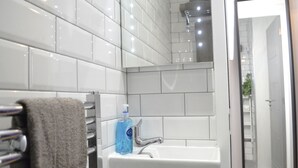 Um banheiro com azulejos brancos, porta-toalhas, pia com sabonete líquido e espelho.