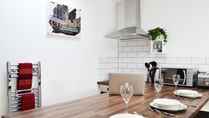 Cozinha moderna com mesa de jantar de madeira para quatro pessoas, forno embutido e planta pendente.