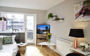 A modern living room with a bed, a TV, a coffee table, and a radiator.