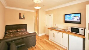 A compact room with a bed, a kitchenette, and a TV mounted on the wall. - Central Studios Gloucester Road by Rooms Booked - Free Parking (Cheltenham)