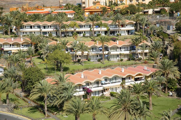 Un resort con varias villas de dos pisos, cada una con techo curvo y rodeada de palmeras.