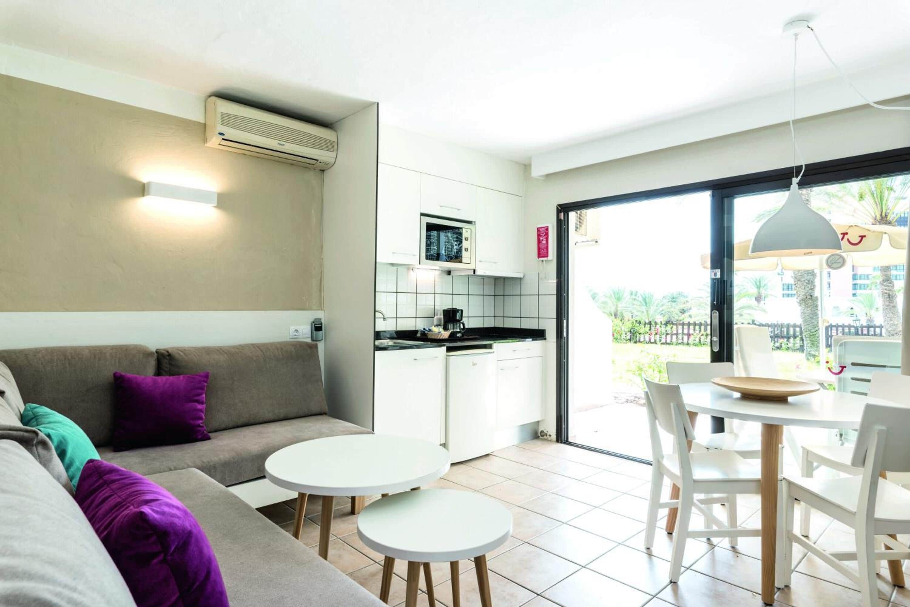 Un espacio habitable moderno con un sofá, dos mesitas, una cocina y una mesa de comedor con sillas.