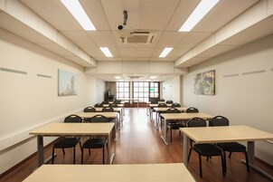 Sala de conferência com várias mesas e cadeiras, amplas janelas e projetores instalados no teto.