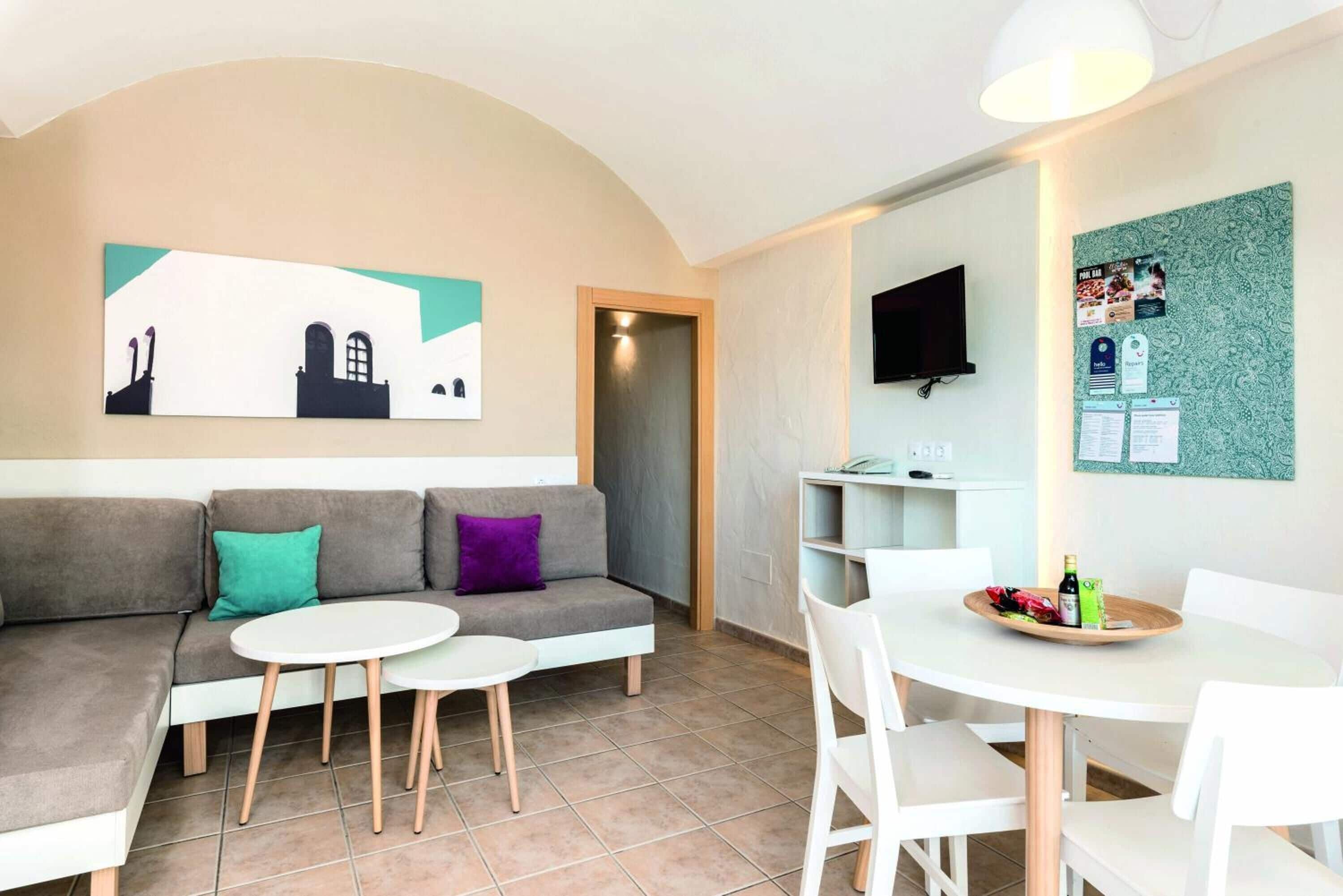 Een moderne woonkamer met een bank, twee kleine ronde tafels en een aan de muur bevestigde televisie.