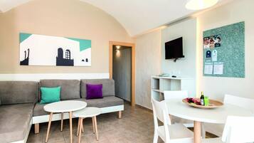 Een moderne woonkamer met een bank, twee kleine ronde tafels en een aan de muur bevestigde televisie.