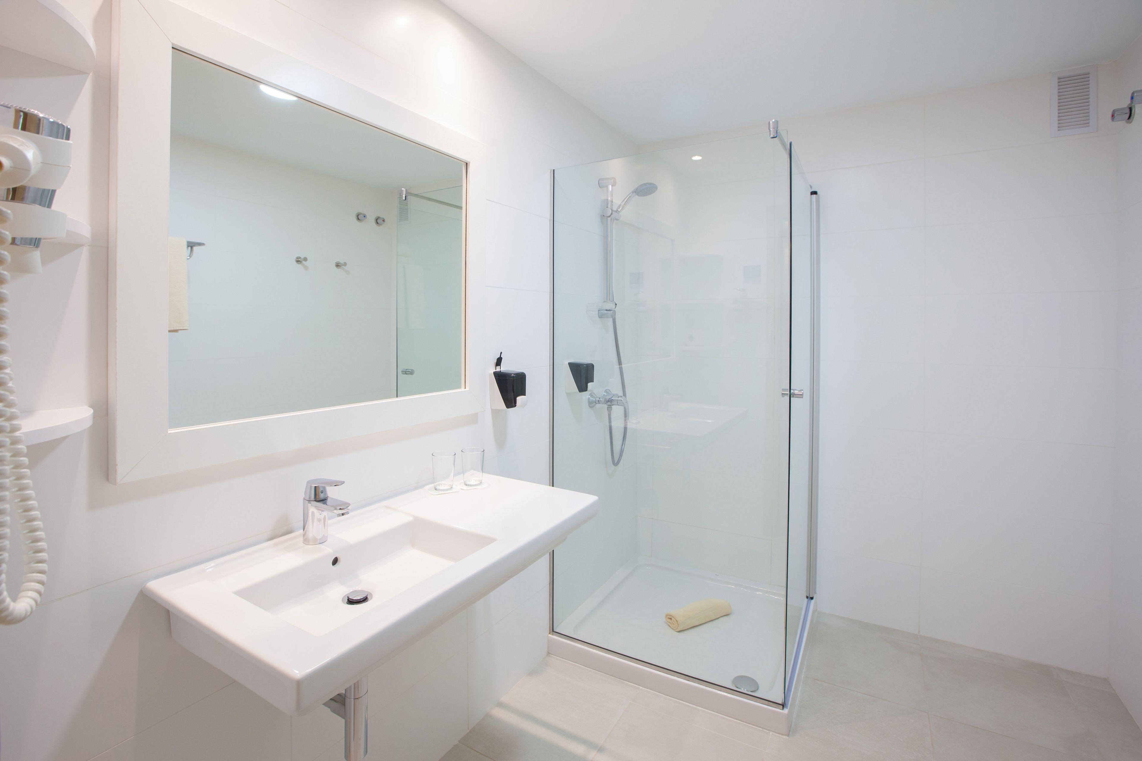 A modern bathroom with a glass-enclosed shower, a white sink, and a large mirror.