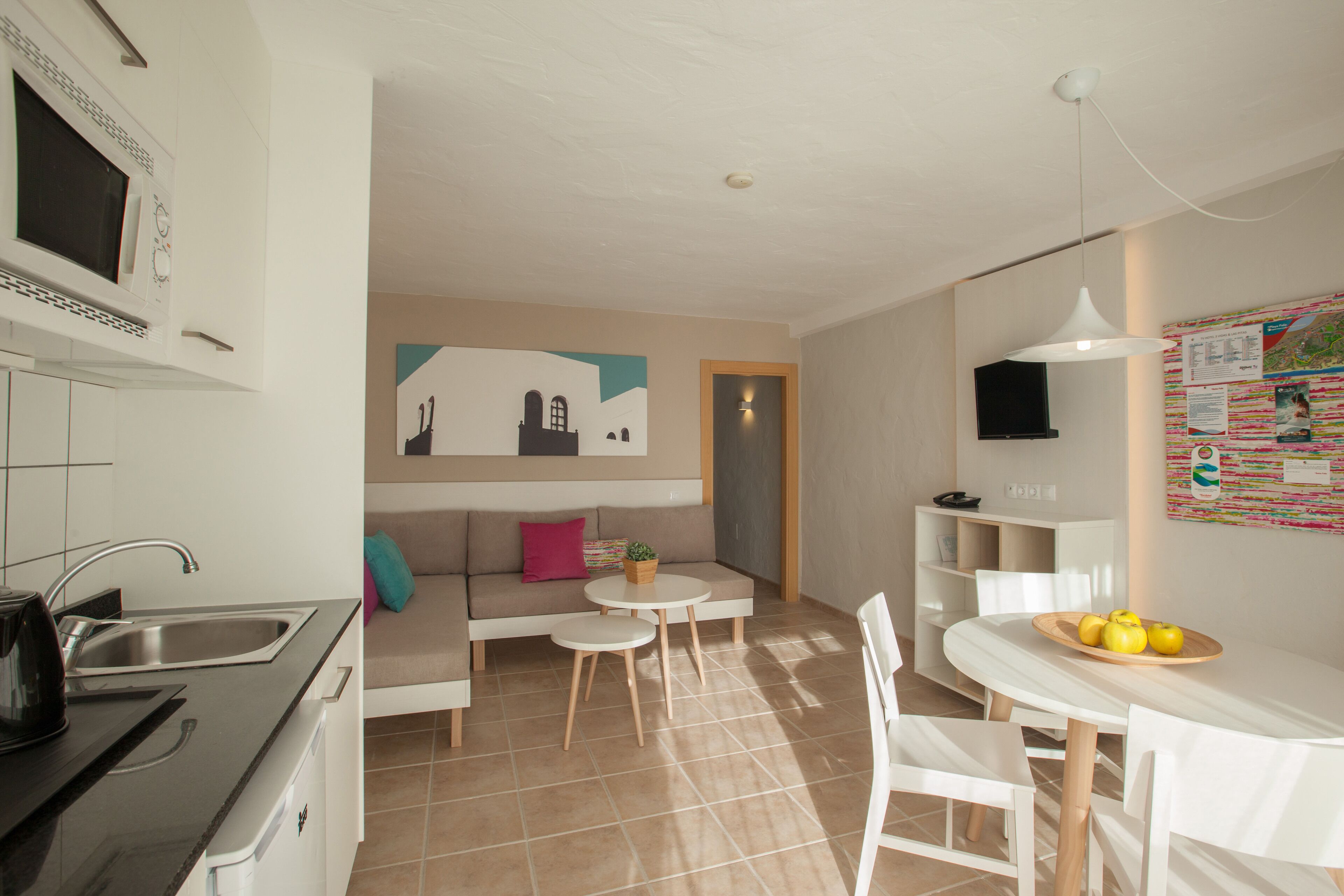A modern kitchen with a sink and stove, a dining area with a table and chairs, and a living area with a sofa and a small table.
