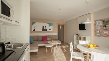 A modern kitchen with a sink and stove, a dining area with a table and chairs, and a living area with a sofa and a small table.