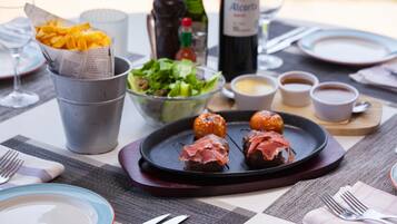 Una mesa preparada para una comida, con un plato de albóndigas, una cesta de papas fritas, una ensalada y una botella de vino.