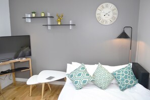 A bedroom with a bed, a TV, a desk, and shelves with decorative items.