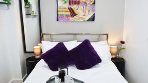 Una cama bien hecha, adornada con almohadas moradas, una cafetera y una bandeja con tazas y una tetera.