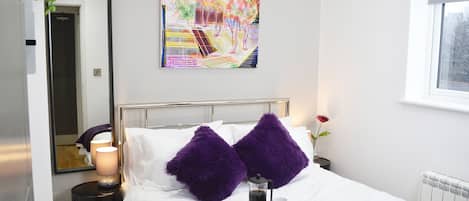 A modern hotel room with a neatly made bed, a coffee table with a tray, a painting on the wall, and a window with a view.