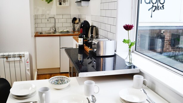 Una cocina moderna con comedor, que cuenta con un ventanal con vistas a la ciudad, un tostador y un florero con una flor en la mesa.