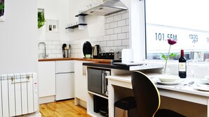 Una cocina moderna con armarios blancos, una encimera negra y una ventana que ofrece vistas a un edificio con la señalización "101.5FM".