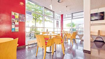 A modern interior with round tables and wooden chairs, large windows, and a red accent wall.
