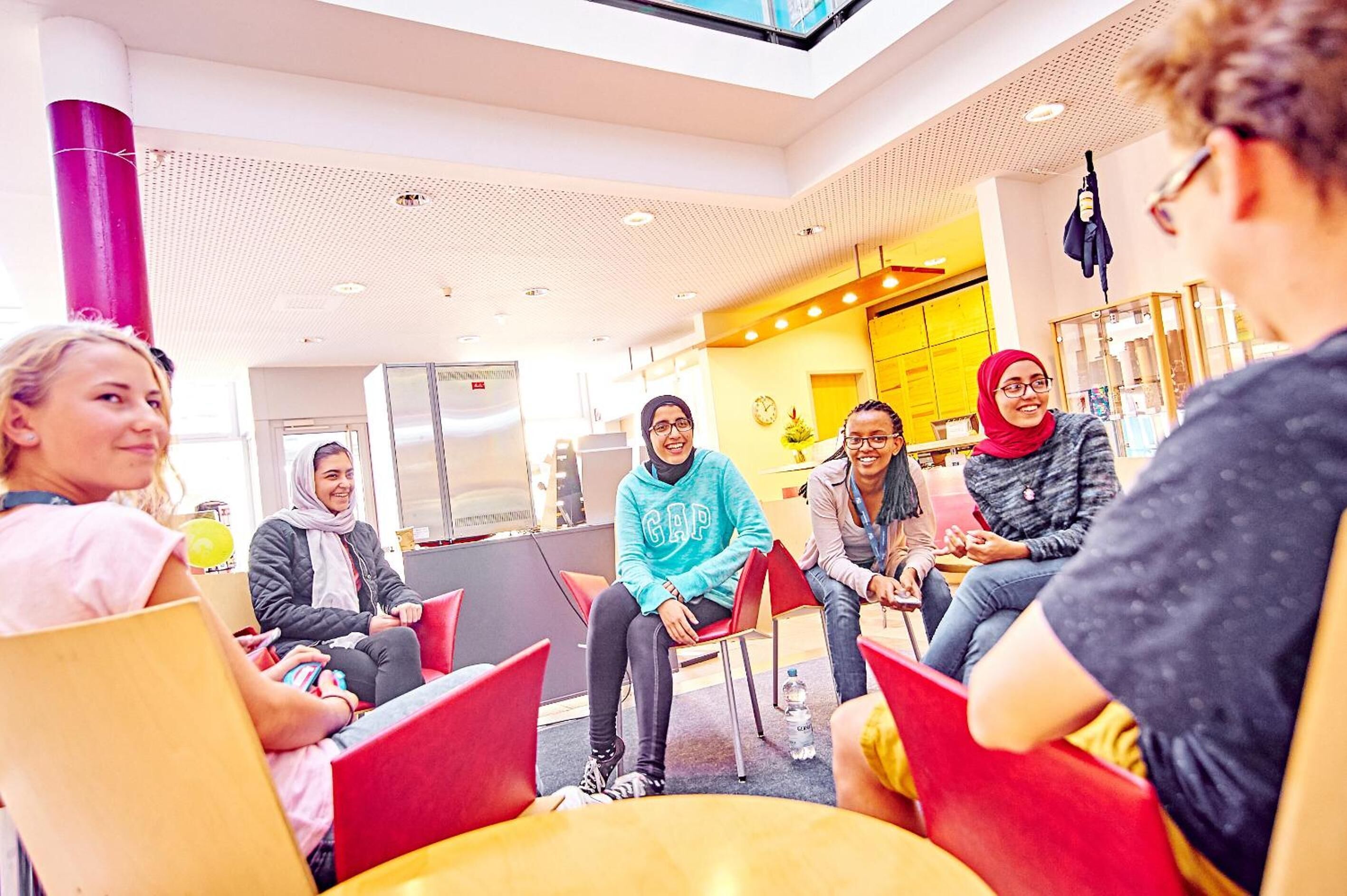 A group of people seated in a modern indoor space with a high ceiling and bright lighting.
