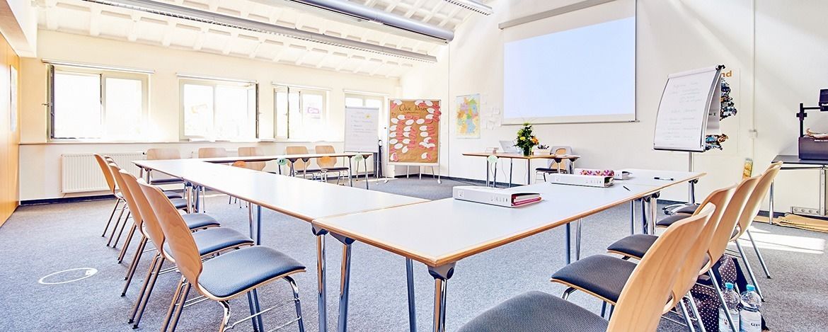 Una sala de conferencias con una larga mesa, sillas, una pizarra y una pantalla para proyector.