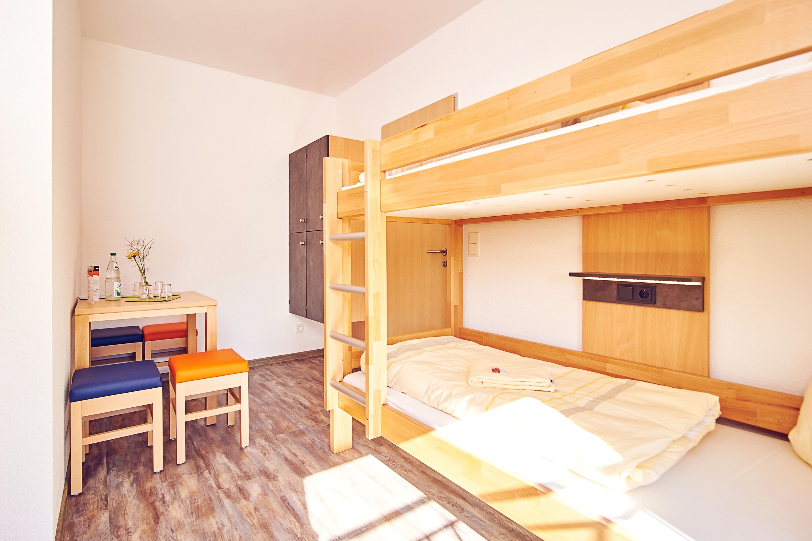 Habitación con literas, un escritorio, una silla, un armario y una pequeña mesa con objetos encima.