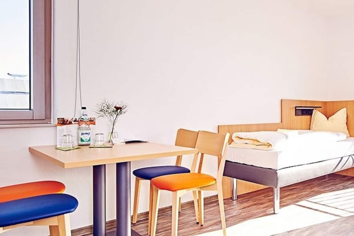 A hotel room with a bed, a desk, and two chairs. There is a window with a view of greenery.
