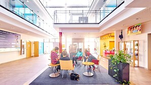 Un espace intérieur moderne doté d’un haut plafond, de rampes en verre et d’un espace de détente central avec des tables et des chaises rondes.