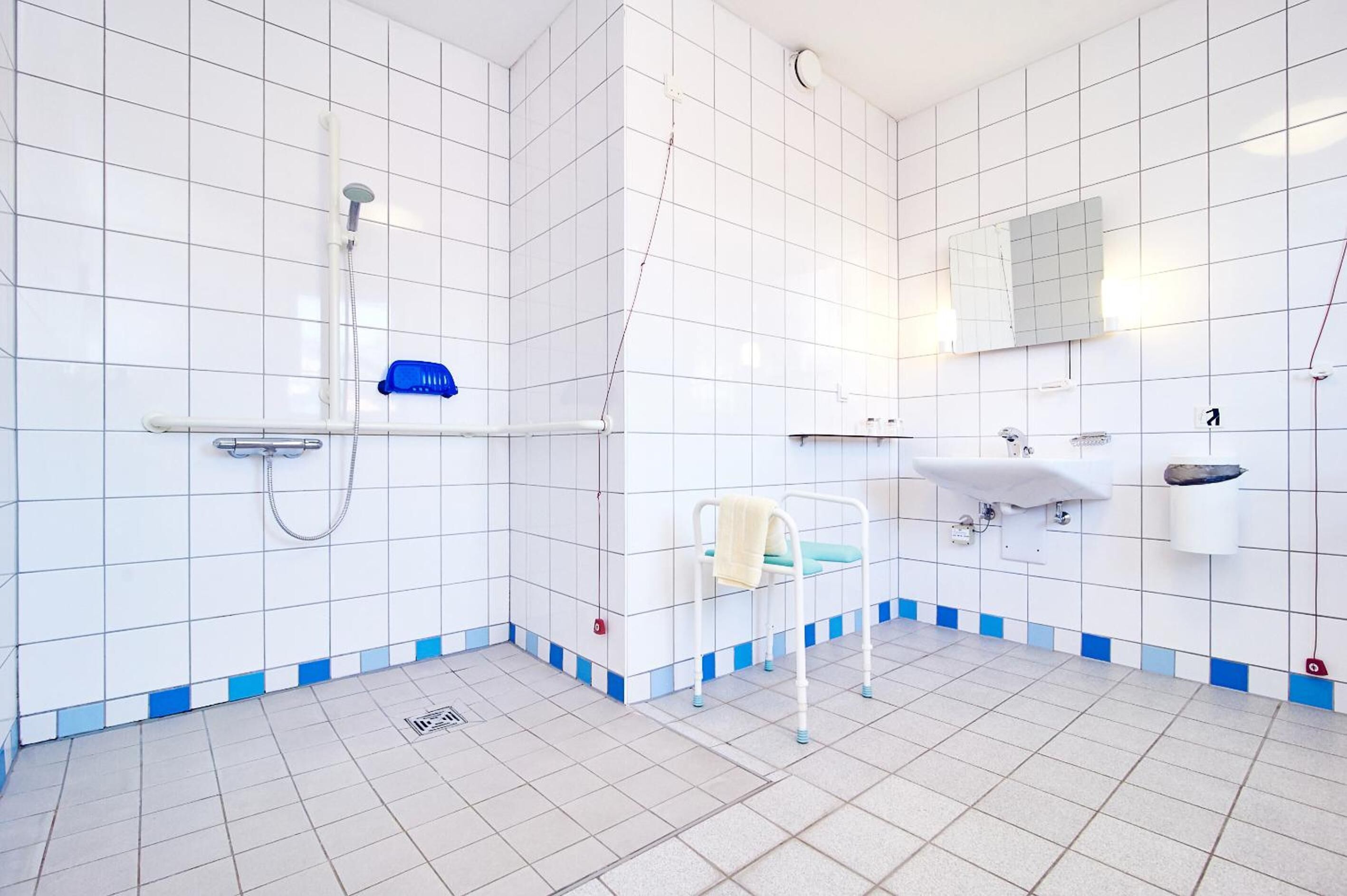Ein modernes Badezimmer mit weißen Fliesen, einer Dusche, einem Waschbecken und einem Spiegel.