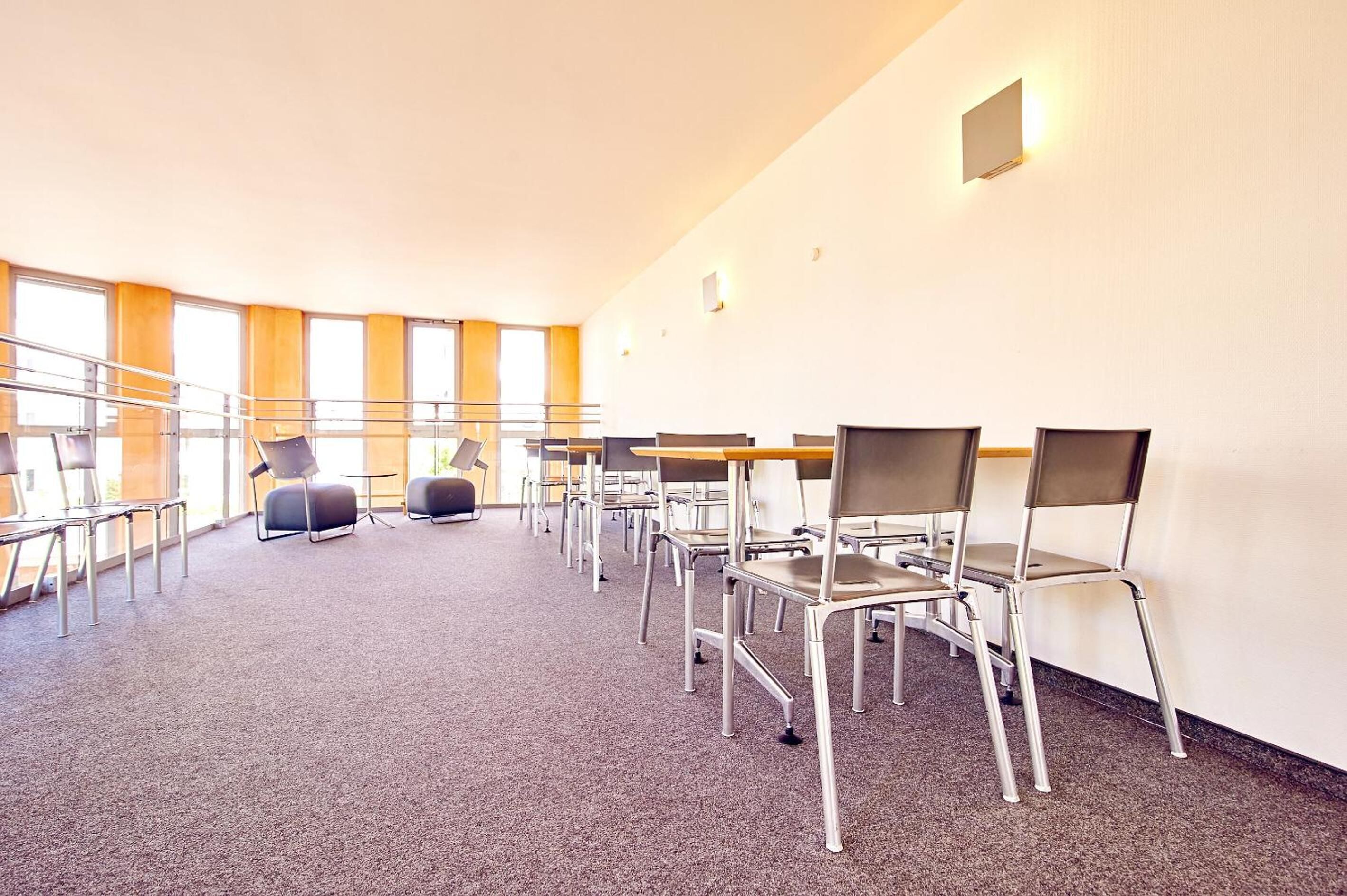 Un salón de conferencias con filas de sillas y mesas, ventanas amplias y piso alfombrado.