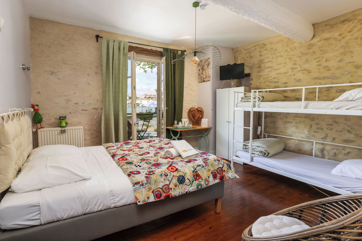 A bedroom with a single bed, a bunk bed, a wicker chair, and a view of the city through a window.