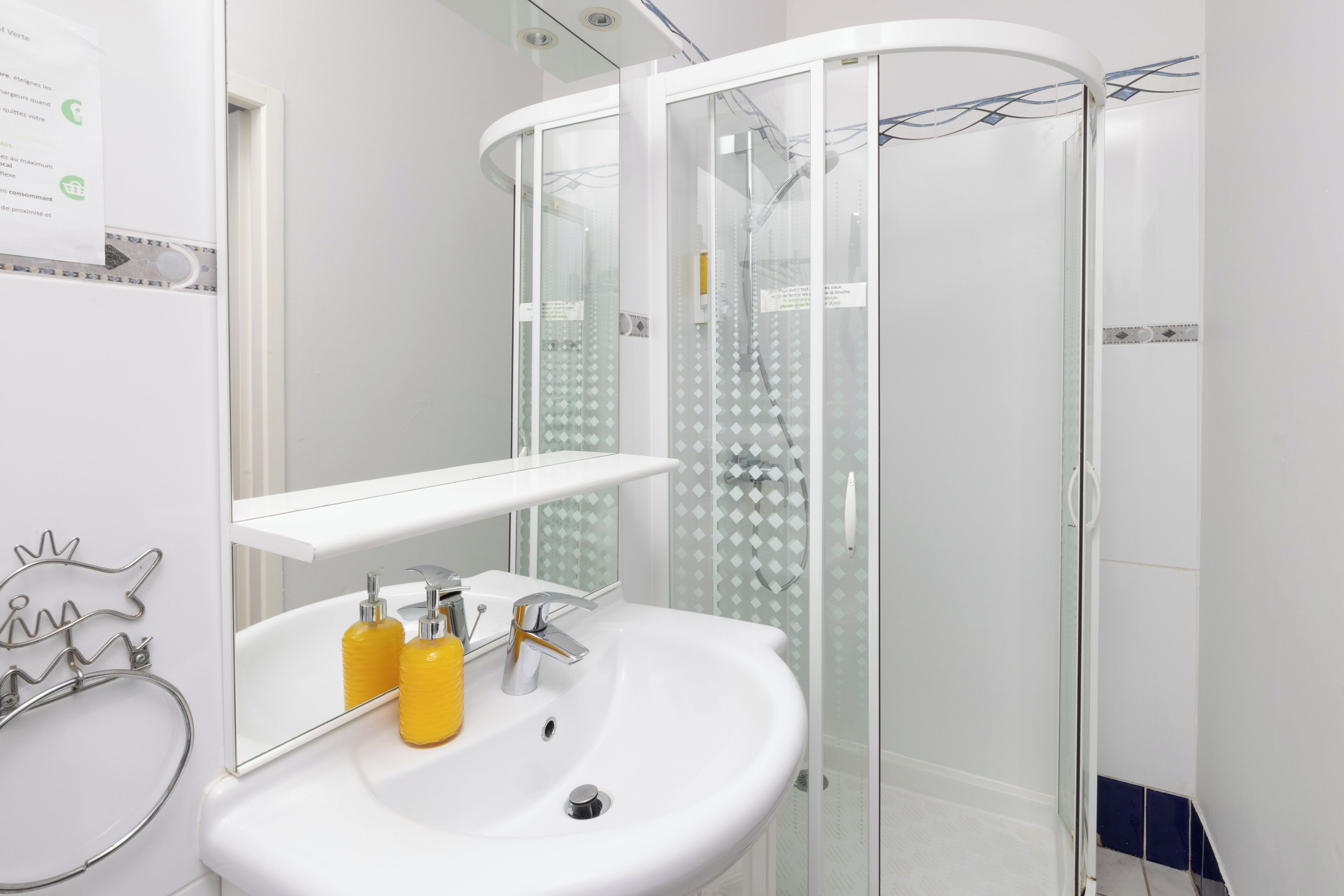A modern bathroom with a white sink, mirror, and glass shower enclosure.