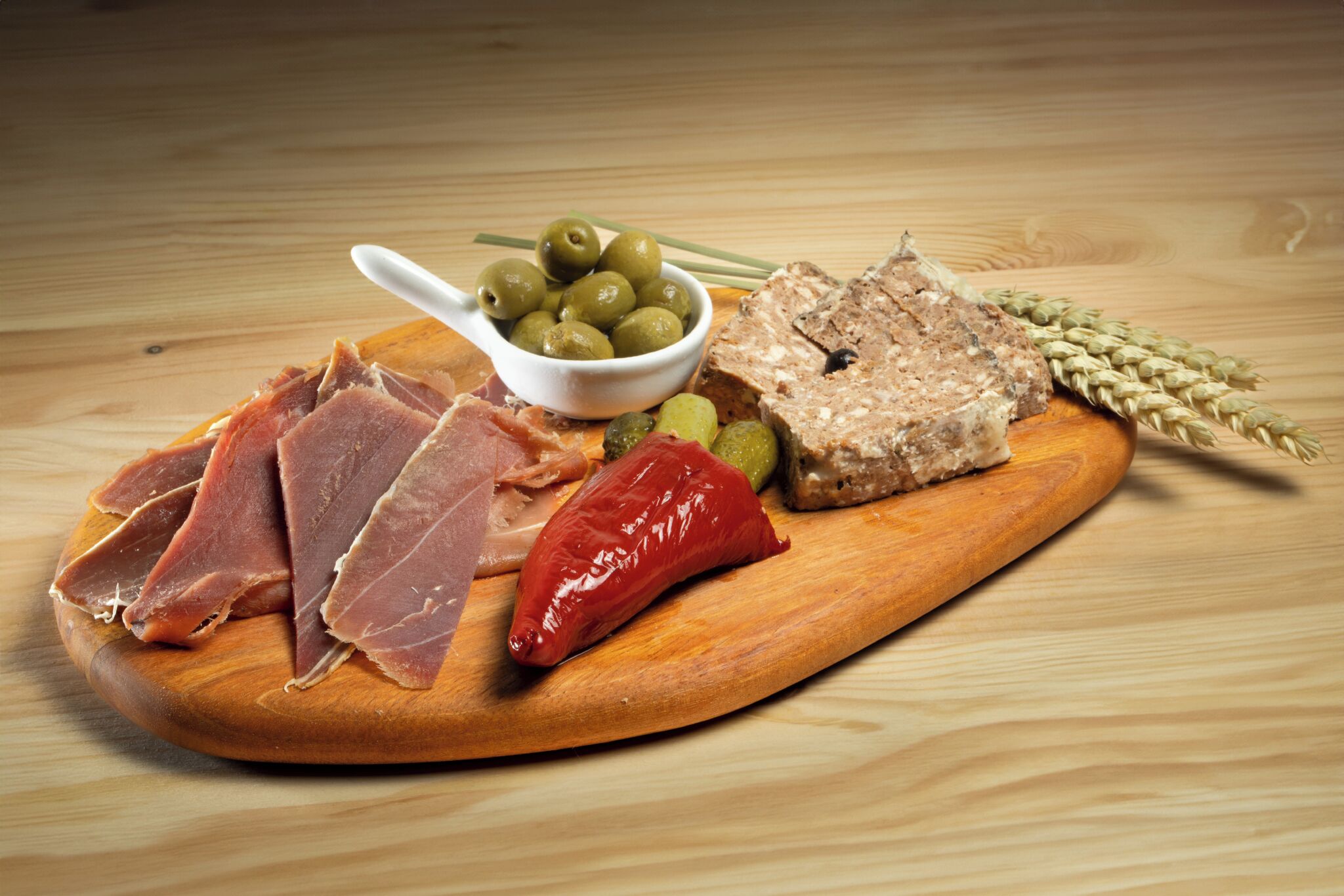 Une planche en bois sur laquelle sont disposés divers aliments, notamment des olives, un piment rouge et un morceau de viande.